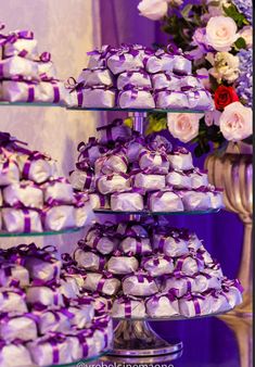 there are many small cakes that are stacked on the table with purple ribbons and bows