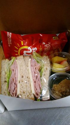 a sandwich with meat, lettuce, and fruit in a take out box