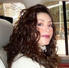 a woman sitting in the back seat of a car with long curly hair and blue eyes