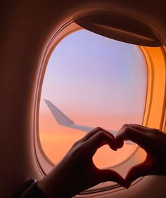 a person making a heart shape with their hands in front of an airplane window