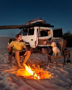 a man sitting in front of a camper van next to a dog on the beach