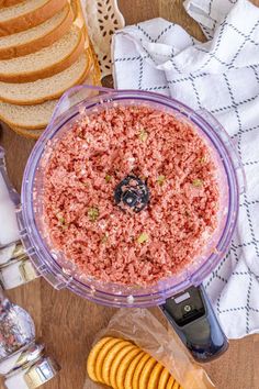 a food processor filled with ground meat next to sliced bread and crackers on a table