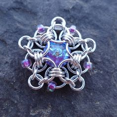 a silver ring with blue and purple beads on it sitting on top of a rock