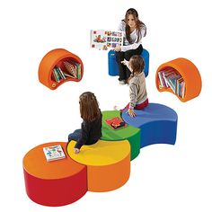 three children sitting on different colored tables and chairs with bookshelves in the background