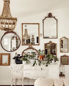 a white dresser topped with lots of mirrors next to a wall filled with framed pictures