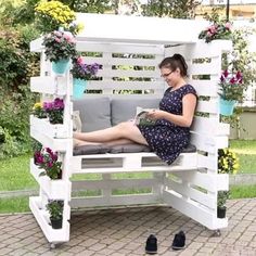 a woman is sitting on a bench made out of pallet wood and has potted plants