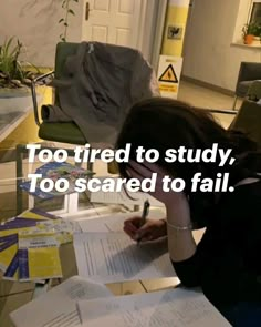 a woman sitting at a table with papers and pens in front of her, reading too tired to study, too scared to fail