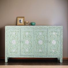 a green cabinet with white flowers painted on the front and sides, next to a framed photograph