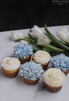 cupcakes with white frosting and blue flowers on a marble countertop next to tulips