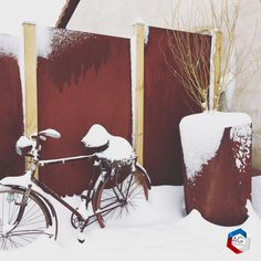 a bicycle is parked in the snow next to a red fence and tall planters