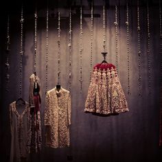 several different types of clothing hanging from chains on a wall in a room with beaded necklaces