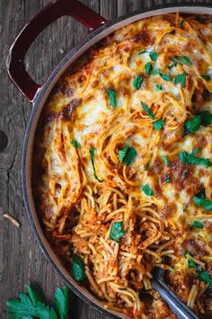 a large pot filled with spaghetti and sauce on top of a wooden table next to parsley