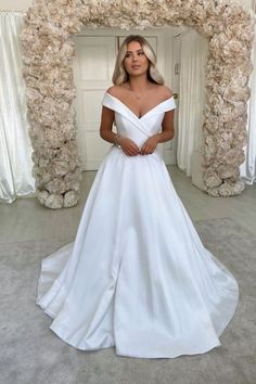 a woman standing in front of a doorway wearing a white wedding dress with off the shoulder sleeves