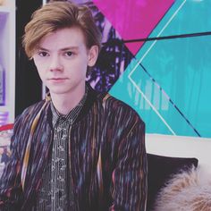 a young man sitting on top of a bed in front of a colorful wallpaper