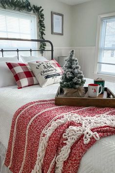 a white bed topped with a red blanket next to two christmas trees and other holiday decorations