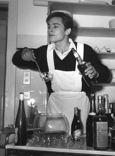 a man in an apron is pouring something into a glass while standing behind some bottles