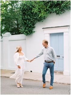 a man and woman are holding hands while walking down the street in front of a white building