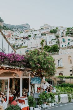 people sitting at tables in front of a building with flowers growing on the side of it