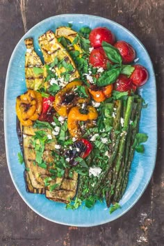 a blue plate topped with grilled vegetables on top of a wooden table next to a fork