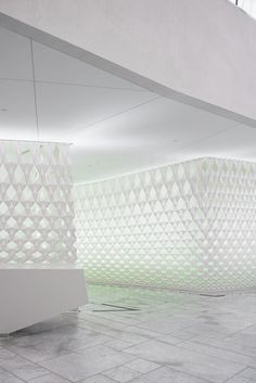 a white bench sitting in the middle of a room next to a tall wall with geometric designs on it