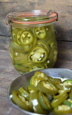 pickled jalapenos in a glass jar next to a metal bowl on a wooden table