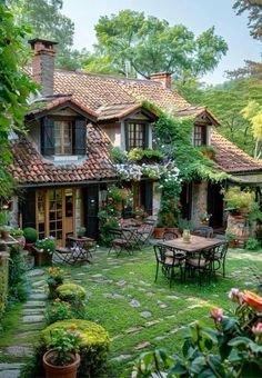 an outdoor patio with tables and chairs in front of a small house surrounded by greenery