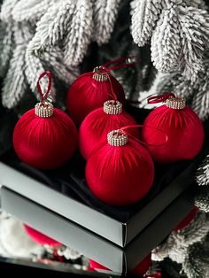 three red ornaments sitting on top of a book next to christmas tree branches and pine cones