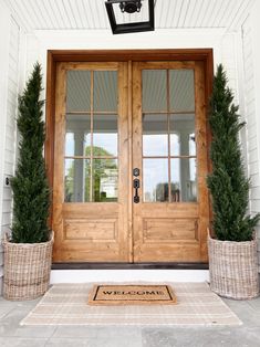 two large potted plants are on the front steps of a white house with wooden doors