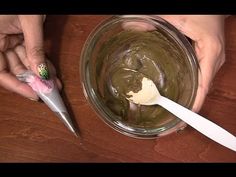 two hands holding spoons over a bowl filled with green liquid and ice cream on top of a wooden table