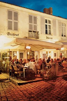 people are sitting at tables outside in front of a building with white awnings