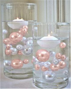 two glass vases with candles in them on a white tableclothed surface, one is filled with balls and the other has an ornament