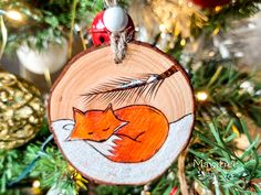 a wooden ornament with an orange fox sleeping on it's side hanging from a christmas tree