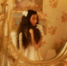 a woman in a white dress looking into a mirror with her hair blowing in the wind