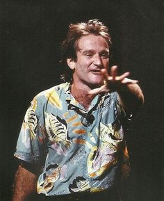 a man with his hand in the air while wearing a hawaiian shirt and black pants