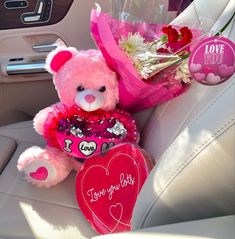 a pink teddy bear sitting in the back seat of a car holding a heart shaped bouquet