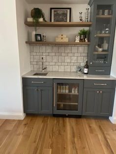 a kitchen with gray cabinets and white tile backsplashing, wood floors and open shelving above the sink