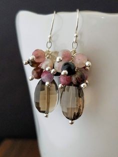 These stunning earrings feature large beautifully faceted Smokey Quartz and faceted Tourmaline hand wrapped with sterling silver wire to sterling silver chain. The ear wires are also sterling silver. These boho inspired statement earrings are sure to please! They have great sparkle and movement. The earrings in the pictures are the exact pair you will receive. Your earrings will be beautifully wrapped in a black gift box with ribbon.  The earring length is approx. 1.5 inches. Tourmaline is said Smokey Quartz Earrings, Gift Box With Ribbon, Silver Chandelier Earrings, Lotus Earrings, Box With Ribbon, Handmade Jewelry Designs, Black Gift Boxes, Black Gift, Quartz Earrings