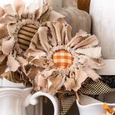 a coffee cup filled with burlap flowers on top of a shelf next to a vase