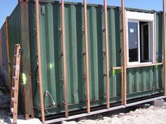 a green shipping container sitting on top of a pile of dirt next to a window