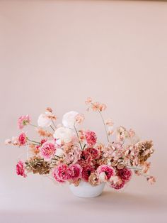 a white vase filled with lots of pink and white flowers on top of a table