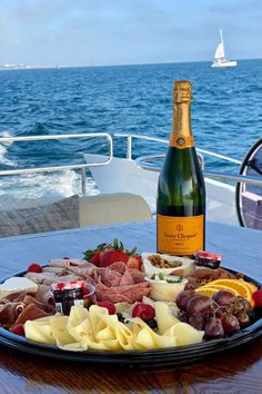 a bottle of champagne and some food on a table near the ocean with a boat in the background