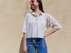 This 80s top has a boxy dolman sleeve fit with a three button collar and faux pocket flaps in a lightweight, breezy fabric with a pretty watercolor pastel plaid. Styled with 1990s handpainted jeans available here: https://www.etsy.com/listing/1702436824/1990s-handpainted-jeans-glitter-purple   55" chest  21" front length 23" back length Modern size Large Sizes as listed on Etsy are my best guess Please always compare to your own measurements for optimal fit Model is 36-29-41 and 5'11" Too Shy! l Vintage Relaxed Fit Cropped Tops, Vintage Cropped Tops With Relaxed Fit, Summer Cropped Shirt With Buttons For Daywear, Retro Blouse With Buttons And Relaxed Fit, Oversized Collared Top For Daywear, Oversized Blue Top With Placket, Oversized Collared Vintage Blouse, Oversized Retro Button-up Top, Retro Oversized Button-up Tops