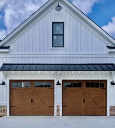 two brown garage doors are open in front of a white house with black trim on the roof