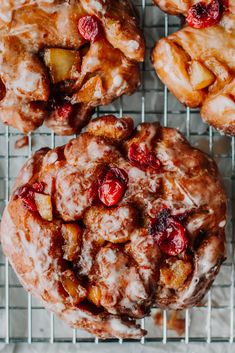 several pastries sitting on top of a cooling rack next to some apples and cranberries