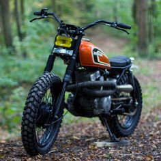 an orange and black dirt bike parked on a trail in the middle of a forest