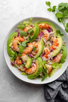 a white bowl filled with lettuce, shrimp and avocado on top of a table