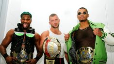 three men standing next to each other with their arms around one another and holding two different wrestling belts