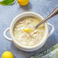 a bowl of chicken and dumpling soup with lemons on the table next to it