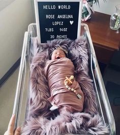 a baby wrapped in a blanket laying on top of a bed next to a sign