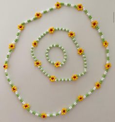 a beaded necklace with yellow and green flowers on white beads next to a spiral design